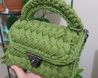 May include: A green crocheted handbag with a top handle and a flap closure. The bag has a fringe detail and a silver metal clasp.