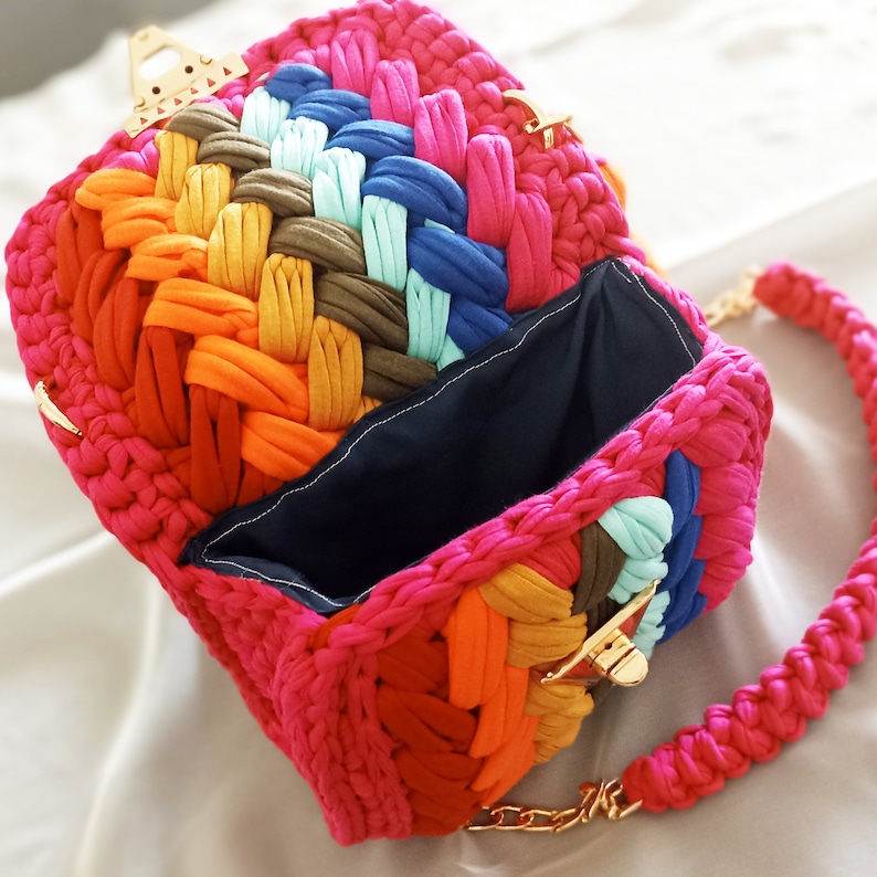 May include: A colorful crocheted bag with a gold clasp and a matching chain strap. The bag is made of different colored yarn, including pink, orange, yellow, green, blue, and brown.