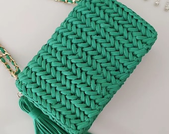 May include: A green woven crossbody bag with a tassel. The bag has a gold chain strap.