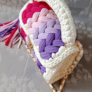 May include: A white crocheted handbag with a gold chain strap. The bag has a multi-coloured striped design with pink, purple, and white yarn.