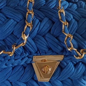 Puede incluir: Un bolso de mano de tela azul con una correa de cadena dorada y un cierre dorado. La tela est&aacute; tejida en un patr&oacute;n de tejido de cesta.