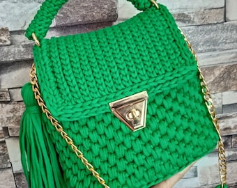 May include: A green crocheted handbag with a gold chain strap and a gold clasp. The bag has a tassel on the side.