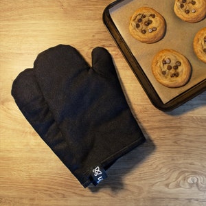 May include: Black oven mitt with a white logo. The mitt is made of a thick, durable fabric and is designed to protect your hands from heat.