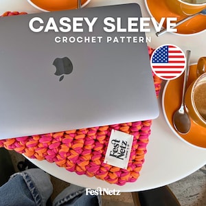 Può includere: Una custodia per laptop in crochet rosa e arancione con il testo "Casey Sleeve Crochet Pattern" e un piccolo cartellino che dice "FestNetz" in testo nero su sfondo bianco. La custodia è su un tavolo bianco con un laptop e una tazza di caffè.