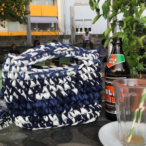 May include: A handmade, rectangular basket with a handle, crafted from thick, woven fabric in alternating shades of navy blue and white. The basket sits on a stone surface, with a bottle of Cola Mix and a glass nearby.