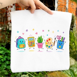 Könnte beinhalten: Ein weißes T-Shirt mit einem bunten Grafikdruck von fünf anthropomorphen Schulutensilien, darunter ein Rucksack, ein Taschenrechner, eine Topfpflanze, eine Farbpalette mit Pinsel sowie ein Stiftehalter mit Schere und Markern, verziert mit Sternen.