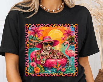 May include: A black t-shirt featuring a square graphic print of a leopard wearing a pink sun hat and sunglasses, lounging on a pink inflatable ring in a tropical pool. The scene includes a pink flamingo, palm trees, and a sunset, all framed by a leopard print border.