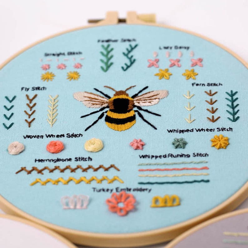 May include: A blue embroidery hoop with a variety of stitches and a bumblebee design. The stitches include fly stitch, woven wheel stitch, herringbone stitch, fern stitch, whipped wheel stitch, whipped running stitch, and turkey embroidery.