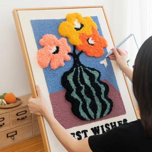 May include: A framed needlepoint canvas with a colorful floral design. The design features three flowers in a vase with the words "Best Wishes" at the bottom.