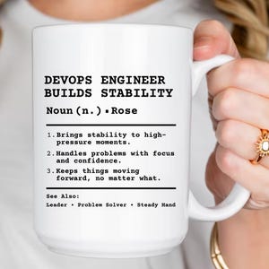 May include: White ceramic mug with the text "DEVOPS ENGINEER BUILDS STABILITY." The mug includes a definition of a DevOps Engineer, highlighting their role in bringing stability, handling problems, and keeping things moving forward.