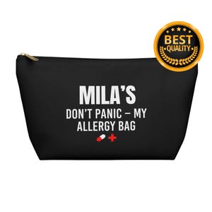 Peut inclure: Pochette zippée noire avec le texte "MILA'S DON'T PANIC - MY ALLERGY BAG" en blanc. Un symbole de croix rouge et de pilule est en dessous. Un sceau doré "BEST QUALITY" est dans le coin supérieur droit.