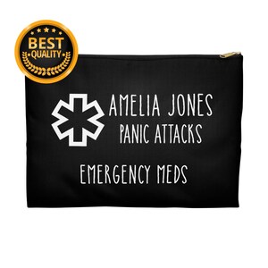 Puede incluir: Bolsa negra con cremallera con texto blanco: «AMELIA JONES PANIC ATTACKS EMERGENCY MEDS». Un símbolo médico blanco está a la izquierda. Un sello dorado de «BEST QUALITY» está en la esquina superior izquierda.