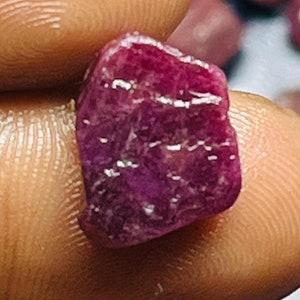 Może przedstawiać: Głęboki różowy rubin o surowym, naturalnym wykończeniu. Rubin ma około 1 centymetra długości i lekko nieregularny kształt.