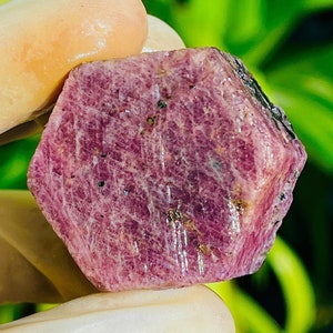 May include: A large, faceted, pink ruby crystal with a hexagonal shape. The crystal has a deep pink color and is translucent.