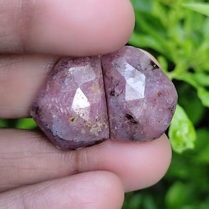 May include: Two pink and purple faceted gemstones with a rough, natural finish.