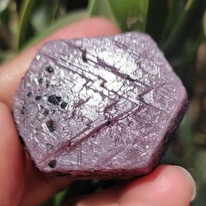 May include: A purple and silver gemstone with a faceted, octagonal shape. The gemstone has a rough, textured surface and is a natural, unpolished crystal.