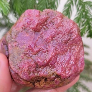 May include: A large, rough, pink ruby gemstone with a textured surface.