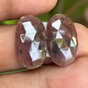 May include: Two faceted, oval-shaped, translucent purple gemstones with a silver shimmer.