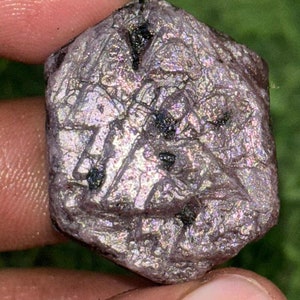 May include: A raw, purple, iridescent gemstone with a rough, faceted surface. The gemstone has a natural, irregular shape and is a beautiful example of a natural crystal.