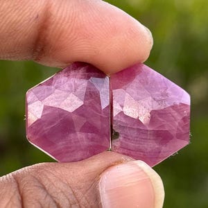 May include: Two pink faceted gemstone cabochons, each with a hexagonal shape and a slightly irregular outline. The stones have a translucent appearance and a deep pink hue.