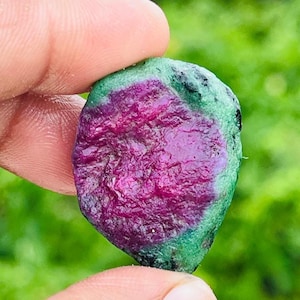 以下が含まれることがあります： 鮮やかなマゼンタピンクの中心部と、質感のある不透明な緑色の縁取りを持つ、未研磨の原石。石は不規則な丸みを帯びた形状で、表面はざらざらしており、結晶のインクルージョンが確認できます。