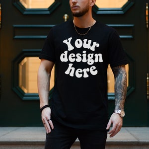 Könnte beinhalten: Ein schwarzes T-Shirt mit dem Text "Your design here" in weißer Schrift im Retro-Stil.