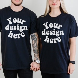 May include: Two black t-shirts with the text "Your design here" in white, retro-style font. The shirts are being modeled by two people.