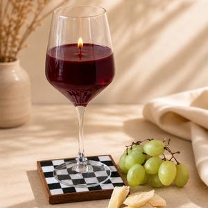 Peut inclure: Une bougie en forme de verre &agrave; vin remplie de cire rouge avec une m&egrave;che allum&eacute;e. La bougie repose sur un dessous de verre &agrave; carreaux noirs et blancs. Des raisins verts et du fromage sont &agrave; c&ocirc;t&eacute; du verre.