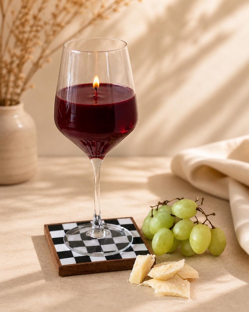 Peut inclure: Une bougie en forme de verre &agrave; vin remplie de cire rouge avec une m&egrave;che allum&eacute;e. La bougie repose sur un dessous de verre &agrave; carreaux noirs et blancs. Des raisins verts et du fromage sont &agrave; c&ocirc;t&eacute; du verre.