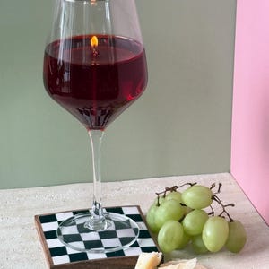 Peut inclure: Une bougie en forme de grand verre &agrave; vin remplie de cire rouge, avec une m&egrave;che allum&eacute;e. La bougie est pos&eacute;e sur un dessous de verre &agrave; carreaux noirs et blancs. Des raisins verts et du fromage sont &agrave; c&ocirc;t&eacute;.