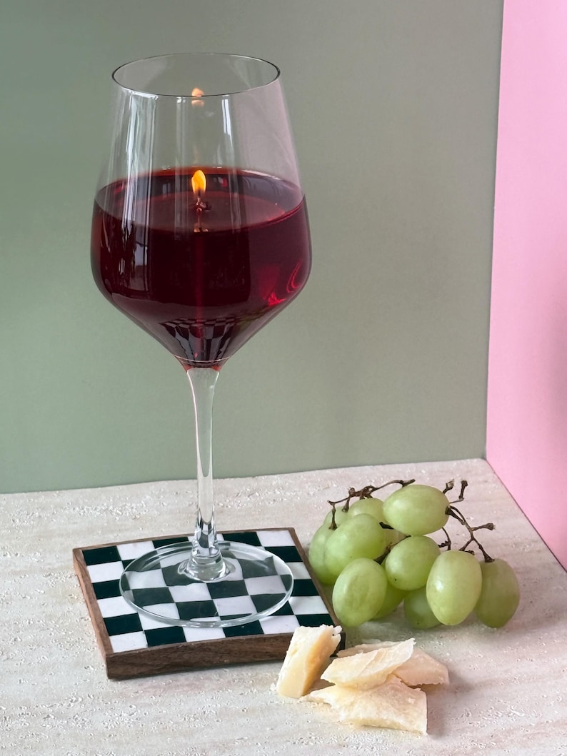 Peut inclure: Une bougie en forme de grand verre &agrave; vin remplie de cire rouge, avec une m&egrave;che allum&eacute;e. La bougie est pos&eacute;e sur un dessous de verre &agrave; carreaux noirs et blancs. Des raisins verts et du fromage sont &agrave; c&ocirc;t&eacute;.