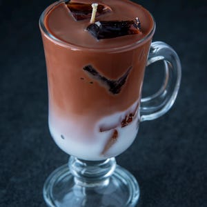 May include: A glass of iced chocolate with a layer of milk and chocolate ice cubes. The drink is topped with a small candle.
