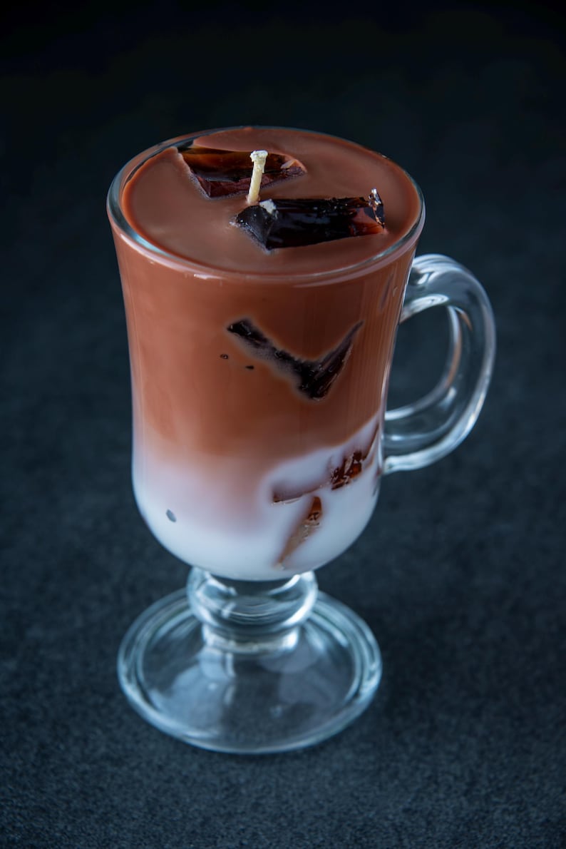 May include: A glass of iced chocolate with a layer of milk and chocolate ice cubes. The drink is topped with a small candle.