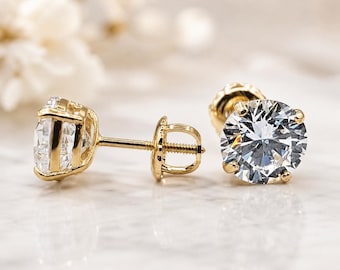 May include: A pair of stud earrings featuring round, clear, faceted stones set in yellow gold. One earring is shown from the side, displaying the post and screw-back mechanism, while the other is positioned to show the front of the stone.