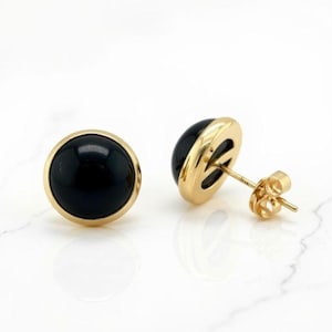 May include: A pair of gold stud earrings featuring a black, round onyx stone. The earrings have a polished gold bezel setting and a post with a butterfly clutch. The earrings are displayed on a white surface.