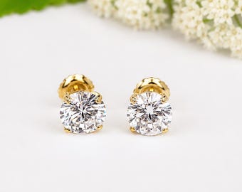 May include: A pair of stud earrings featuring round, brilliant-cut clear stones set in yellow gold prongs. Each earring has a secure gold backing and displays a faceted, reflective surface that catches the light, creating a classic, circular appearance.