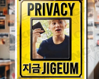 May include: A yellow sign with black text that reads "PRIVACY" and "지금 JIGEU" with a photo of a person in the middle. The sign has a white border and a silver rivet in each corner.