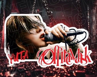May include: A white sticker with a black and white image of a person singing into a microphone. The text "YUTA" is in white letters on the left side of the sticker. The text "Off the Mask" is in red letters on the right side of the sticker.