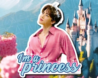 May include: A sticker featuring a person wearing a pink button-down shirt and a silver tiara, with the text "I'm a princess" in a blue font. The background includes a castle, flowers, and mountains.