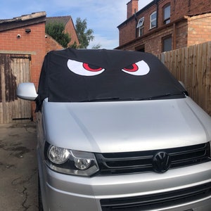 Może przedstawiać: Srebrny van z czarnym grillem i czarno-białą tablicą rejestracyjną z napisem "KW 10 DUB". Van ma czarny osłonę przeciwsłoneczną z dwoma dużymi czerwonymi oczami nadrukowanymi na niej.