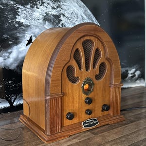 Könnte beinhalten: Ein hölzernes Thomas Collector's Edition Radio mit gewölbter Oberseite, zentralem Lautsprechergitter und einem kleinen beleuchteten Zifferblatt. Die Vorderseite verfügt über drei schwarze Drehknöpfe und ein schwarzes Schild mit der Aufschrift Thomas Collector's Edition Radio.