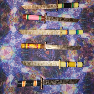 May include: Seven small, decorative knives with patterned blades and colorful handles. The handles are made of wood and have different colored stripes. The blades are made of metal and have a wavy pattern.