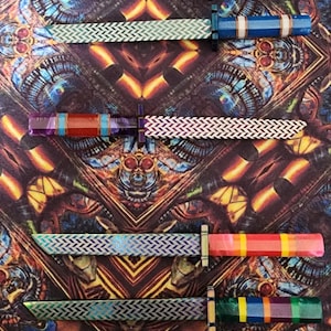 May include: A set of six decorative knives with colorful handles and patterned blades. The handles are made of different materials, including wood, plastic, and metal. The blades are all patterned with a herringbone design.