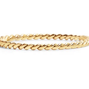 May include: A gold ring featuring a twisted rope design. The thin band has a textured surface created by the twisted pattern. The ring is displayed against a white backdrop.