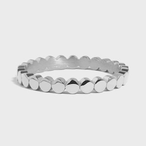Op de afbeelding: Een zilveren ring met een herhalend patroon van kleine, cirkelvormige, gepolijste metalen accenten. De ring heeft een gladde, afgeronde band en een doorlopend ontwerp van gelijkmatig verdeelde cirkels. Een eenvoudig, elegant sieraad.