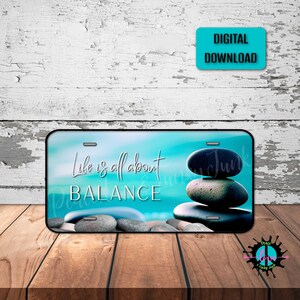 以下が含まれることがあります： ターコイズブルーのナンバープレートに「Life is all about BALANCE」という文字と、ビーチを背景に灰色の石が積み重ねられています。