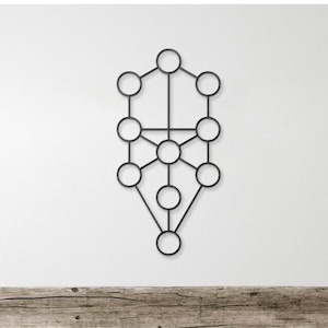May include: Black metal wall art featuring a geometric design of interconnected circles and lines. The artwork is mounted on a white wall above a wooden surface, creating a striking contrast. The design is symmetrical and abstract.