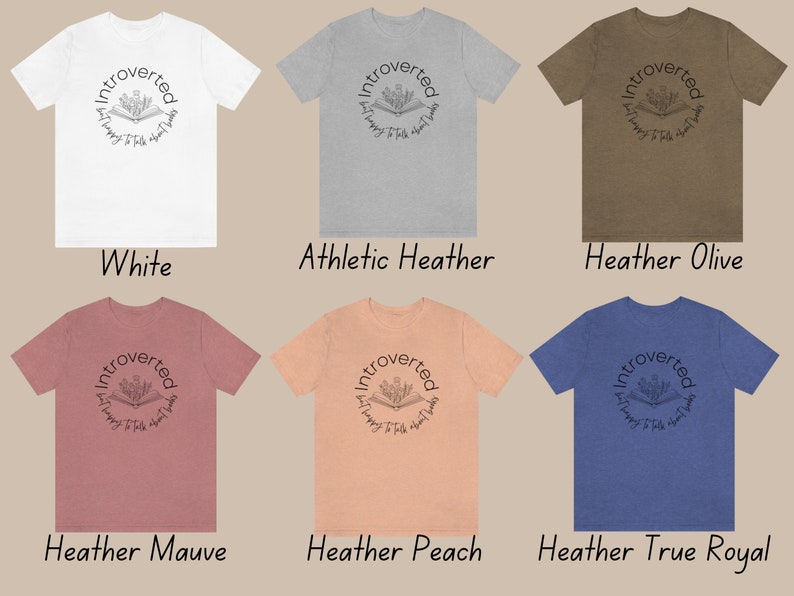 Puede incluir: Seis camisetas de diferentes colores con el texto "Introvertido y feliz de hablar de libros" en un c&iacute;rculo alrededor de un dibujo de un libro abierto con flores que salen de &eacute;l.