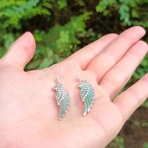 May include: A pair of silver dangle earrings featuring a wing design. The wings are detailed and have a textured surface.