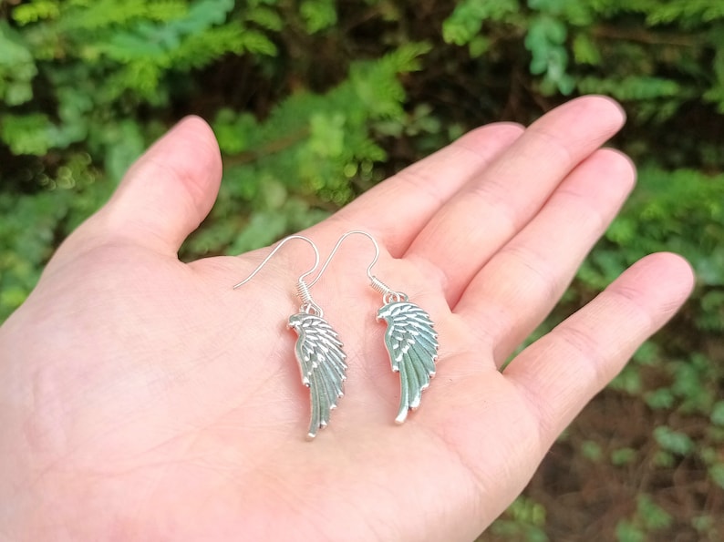 May include: A pair of silver dangle earrings featuring a wing design. The wings are detailed and have a textured surface.
